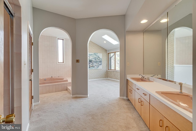 bathroom featuring double vanity, a garden tub, lofted ceiling, and a sink