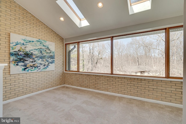 unfurnished room with lofted ceiling with skylight, carpet flooring, recessed lighting, and brick wall