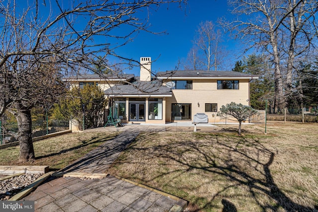 back of property featuring a chimney, french doors, a lawn, a patio area, and brick siding