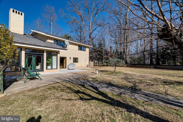 back of house with a patio, a lawn, a chimney, and brick siding