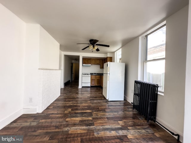 kitchen with under cabinet range hood, white appliances, radiator heating unit, and dark wood-type flooring