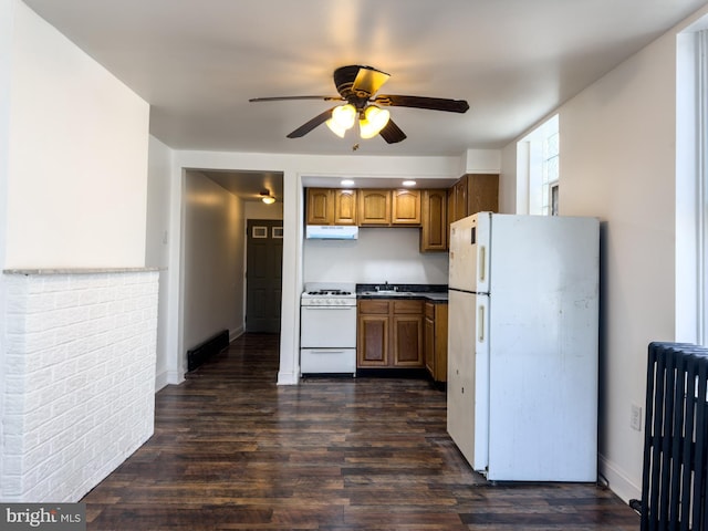 kitchen with brown cabinets, dark wood-type flooring, under cabinet range hood, white appliances, and radiator