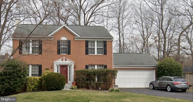 colonial house with driveway, an attached garage, a chimney, a front lawn, and brick siding