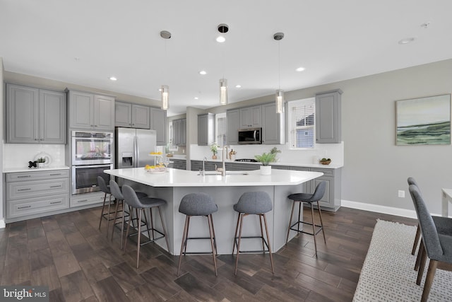 kitchen featuring appliances with stainless steel finishes, light countertops, a kitchen bar, and gray cabinetry