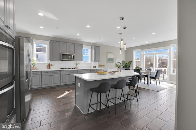 kitchen featuring tasteful backsplash, gray cabinetry, a breakfast bar area, stainless steel appliances, and a sink