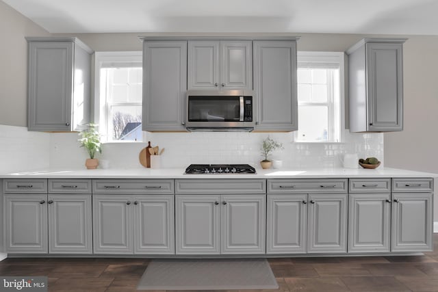 kitchen featuring stainless steel microwave, gray cabinetry, cooktop, light countertops, and decorative backsplash