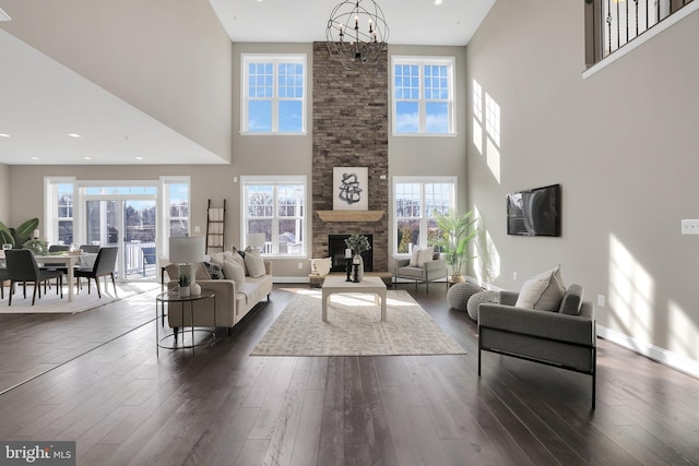 living room featuring a stone fireplace, dark wood-type flooring, a notable chandelier, and baseboards