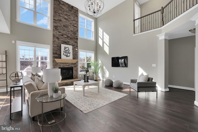 living room with baseboards, a stone fireplace, dark wood finished floors, and an inviting chandelier