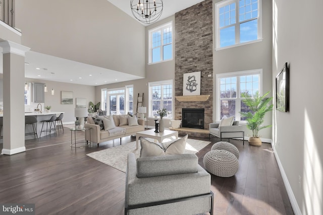 living room featuring baseboards, a stone fireplace, dark wood-style floors, and an inviting chandelier