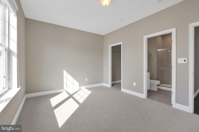 unfurnished bedroom featuring ensuite bathroom, a closet, carpet, baseboards, and a spacious closet