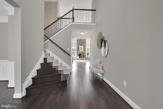 foyer with baseboards, a stone fireplace, wood finished floors, and a towering ceiling