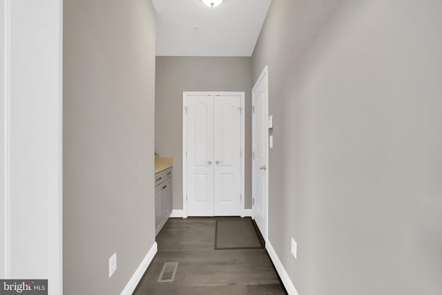 corridor featuring visible vents, baseboards, and dark wood-style flooring