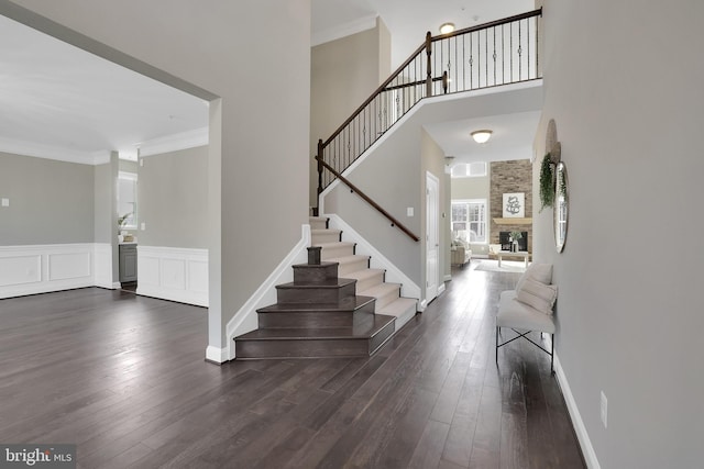 entrance foyer with stairs, a stone fireplace, dark wood-style flooring, and crown molding