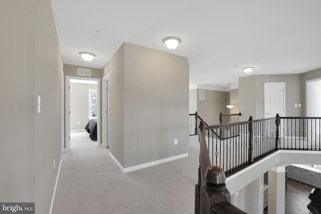 hall featuring visible vents, an upstairs landing, carpet floors, and baseboards