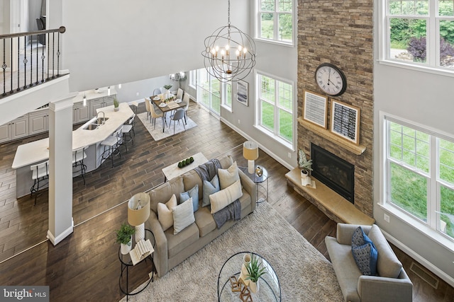 living room with baseboards, dark wood finished floors, a high ceiling, a stone fireplace, and a chandelier