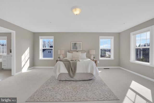 bedroom with baseboards, visible vents, ensuite bathroom, and light carpet