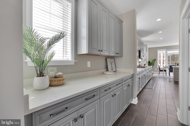 kitchen with gray cabinetry, stainless steel microwave, recessed lighting, light stone countertops, and wood tiled floor