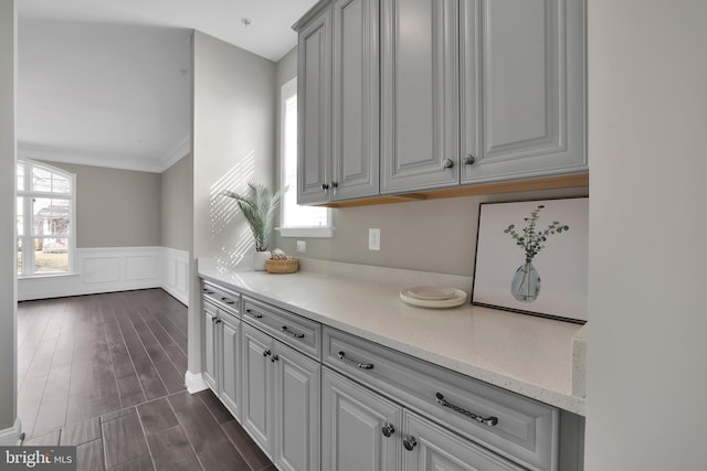 kitchen with light stone counters, dark wood finished floors, wainscoting, a decorative wall, and crown molding