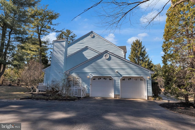 view of side of property with an attached garage, a chimney, driveway, and fence