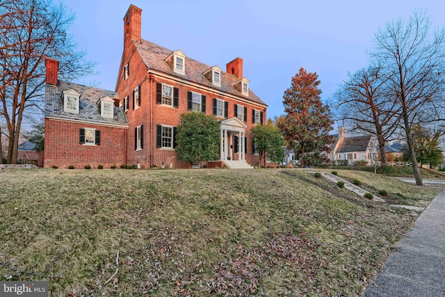 colonial inspired home with a front yard, a high end roof, brick siding, and a chimney