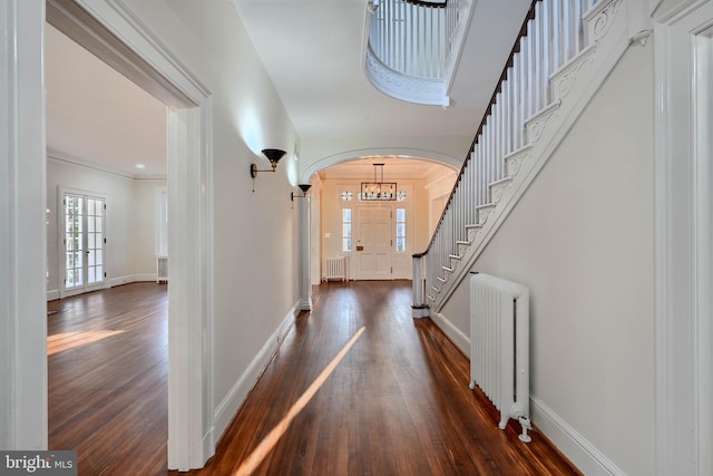 foyer entrance with arched walkways, dark wood finished floors, and radiator heating unit