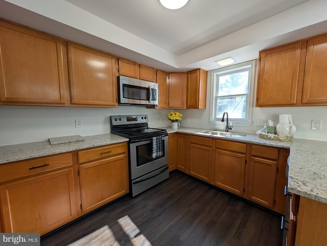 kitchen with light stone counters, a sink, dark wood-type flooring, appliances with stainless steel finishes, and brown cabinets