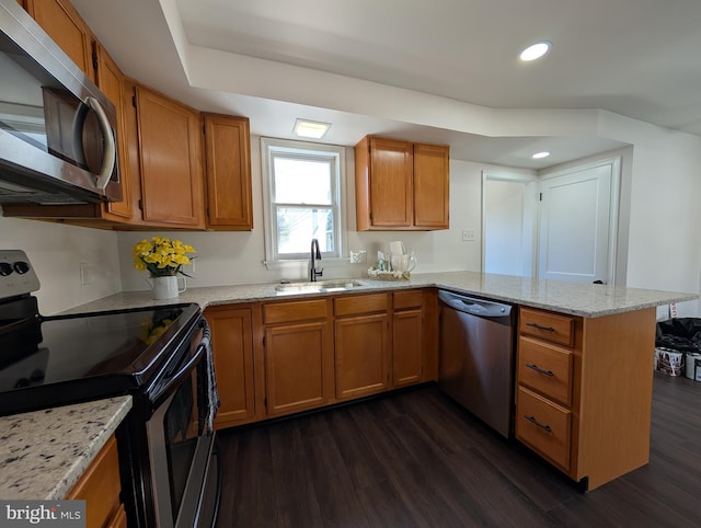 kitchen featuring a peninsula, a sink, dark wood-type flooring, appliances with stainless steel finishes, and brown cabinets