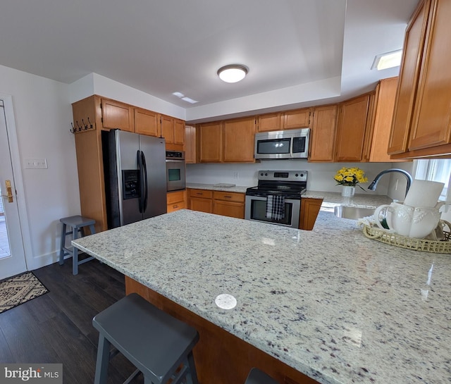 kitchen with a sink, appliances with stainless steel finishes, a peninsula, light stone countertops, and dark wood-style flooring