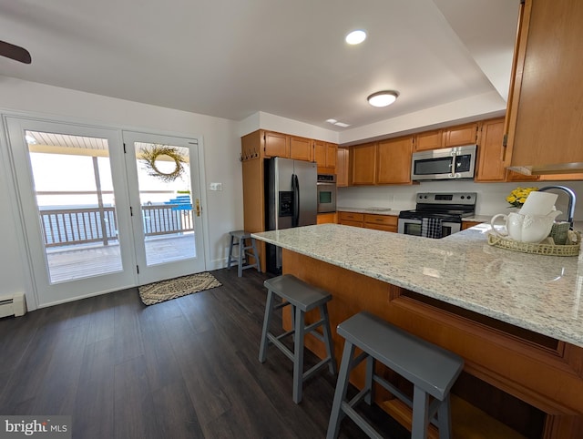 kitchen with dark wood finished floors, light stone counters, brown cabinets, a peninsula, and stainless steel appliances