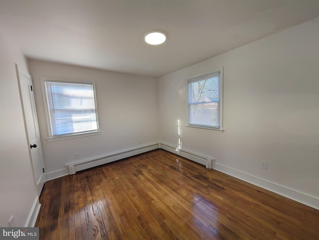 spare room featuring baseboard heating, baseboards, and wood-type flooring