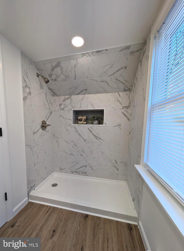 bathroom featuring a wealth of natural light, baseboards, tiled shower, and wood finished floors