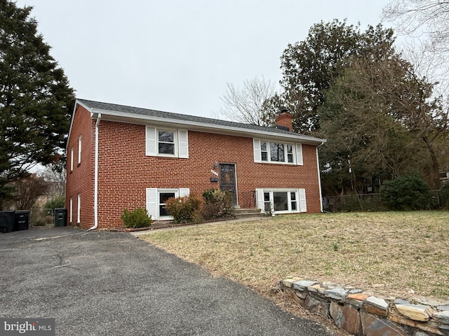 raised ranch with brick siding, a chimney, a front lawn, and fence