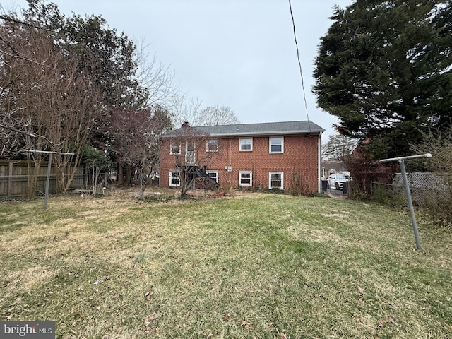 back of property featuring a yard, fence, brick siding, and a chimney