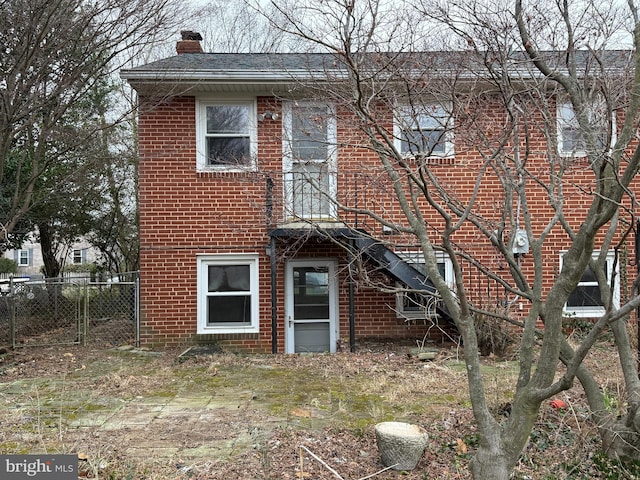 rear view of property with brick siding, a chimney, and fence