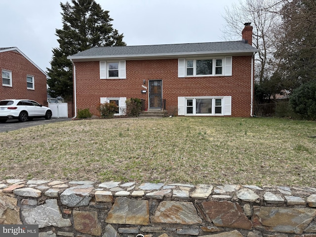 bi-level home with brick siding, a chimney, and a front yard