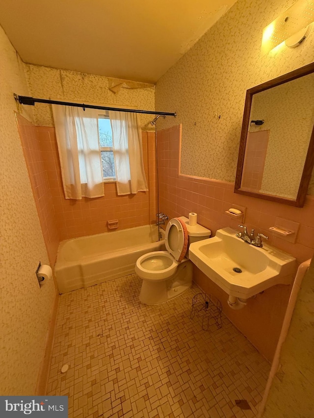 bathroom featuring wallpapered walls, a sink, wainscoting, tile walls, and toilet