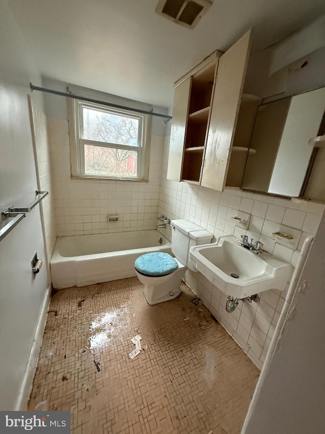 bathroom featuring visible vents, a sink, tile walls, toilet, and shower / bathtub combination