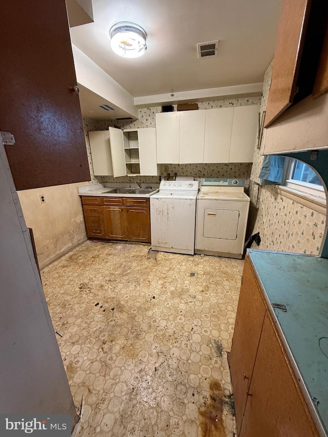 kitchen with visible vents, washing machine and dryer, light floors, white cabinetry, and a sink