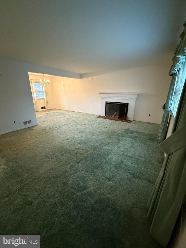 unfurnished living room featuring visible vents, a fireplace with flush hearth, a notable chandelier, and carpet flooring