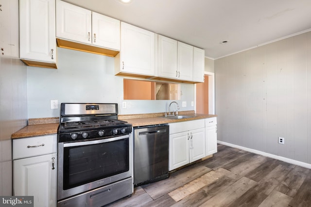 kitchen with wood finished floors, a sink, stainless steel appliances, white cabinets, and crown molding