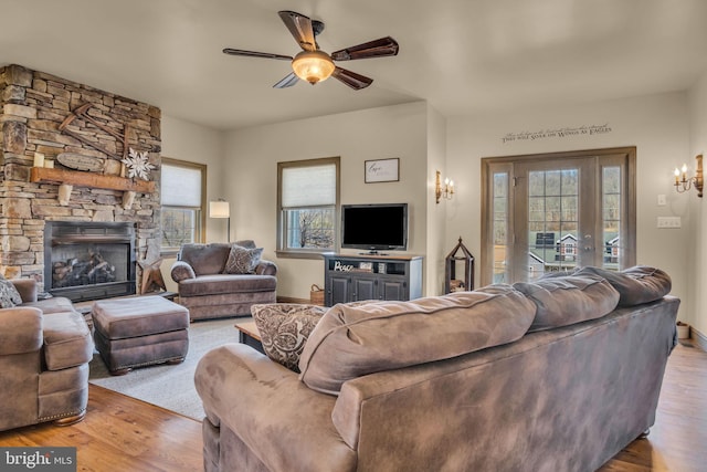 living area featuring a stone fireplace, ceiling fan with notable chandelier, wood finished floors, and baseboards