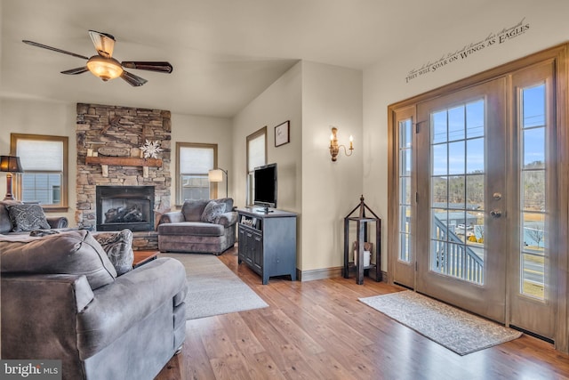 living area with a fireplace, a ceiling fan, light wood-type flooring, and baseboards