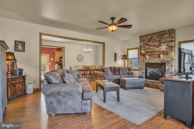 living room featuring a fireplace, ceiling fan with notable chandelier, wood finished floors, and baseboards