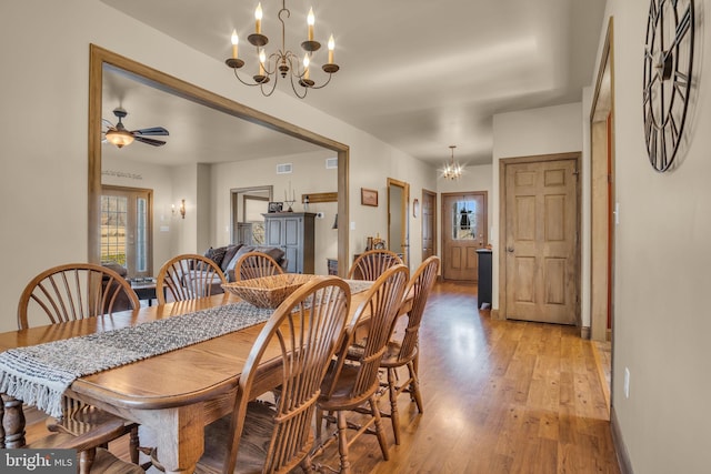 dining space featuring ceiling fan with notable chandelier, visible vents, light wood-style floors, and baseboards