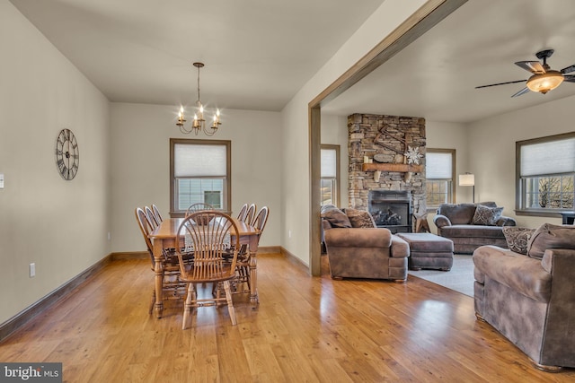 dining room with light wood finished floors, ceiling fan with notable chandelier, a fireplace, and baseboards