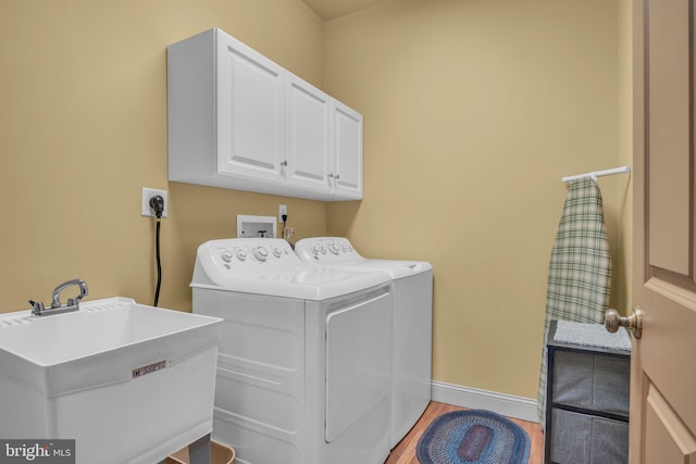 laundry room with baseboards, cabinet space, a sink, washing machine and dryer, and light wood-type flooring