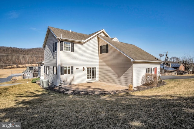 rear view of house featuring a patio area, central air condition unit, a lawn, and a shingled roof