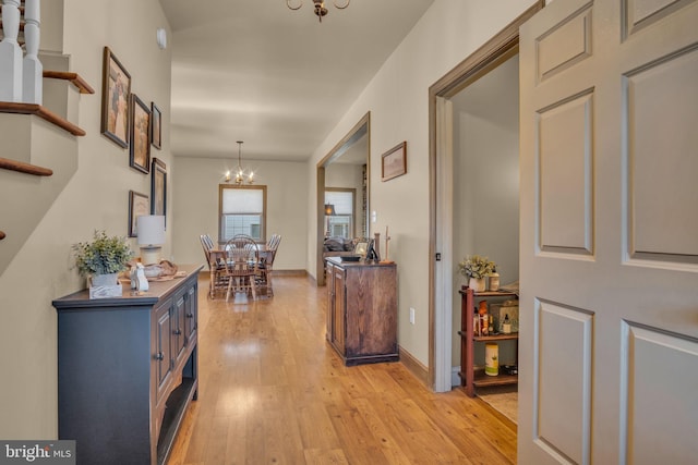 corridor featuring an inviting chandelier, baseboards, and light wood-type flooring