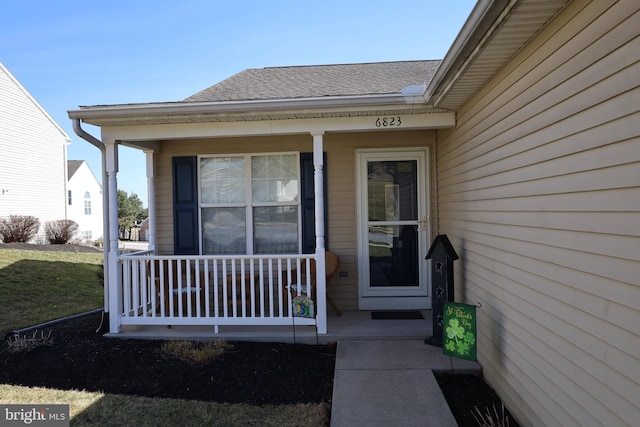 doorway to property with covered porch and a shingled roof