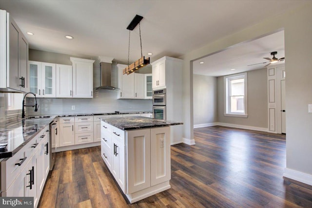 kitchen featuring a sink, dark stone counters, appliances with stainless steel finishes, and wall chimney range hood